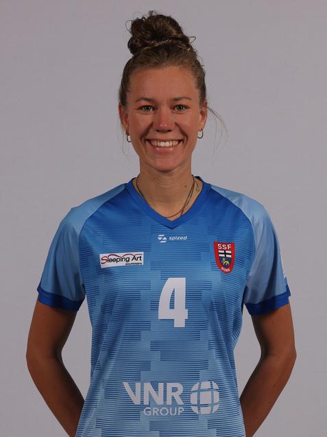 Portr&auml;t einer l&auml;chelnden Frau in einem blauen Sporttrikot mit der Nummer 4 und Sponsorenlogos auf einem neutralen Hintergrund.