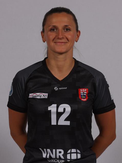 Portr&auml;t einer Frau in einem sportlichen Trikot mit der Nummer 12, l&auml;chelnd vor einem neutralen Hintergrund.