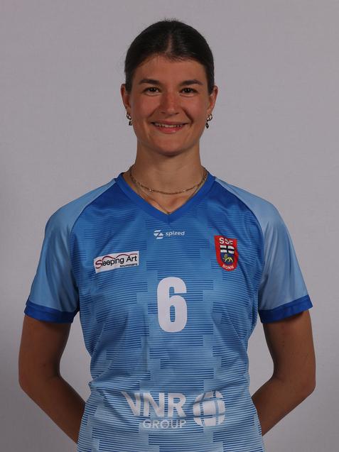 Spielerin in blauem Trikot mit der Nummer 6, l&auml;chelt vor einem einfarbigen Hintergrund.