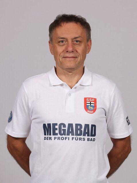 Portr&auml;t eines Mannes in einem wei&szlig;en Poloshirt mit dem Logo "SSF Bonn" und der Aufschrift "MEGABAD DER PROFI F&Uuml;RS BAD".
