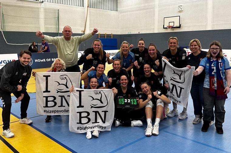 Feiernde Volleyballmannschaft mit Fans, gehaltenen Schildern und Punktzahl 15:32:13 in einer Sporthalle.