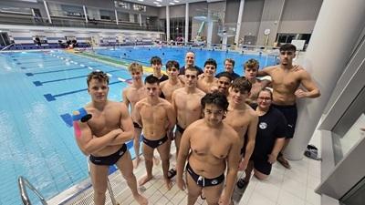 Gruppe von Schwimmern in Badebekleidung posiert am Beckenrand eines Schwimmbades mit blauem Wasser im Hintergrund.