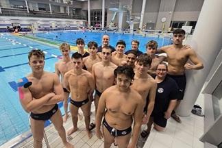 Gruppe von Schwimmern in Badebekleidung posiert am Beckenrand eines Schwimmbades mit blauem Wasser im Hintergrund.