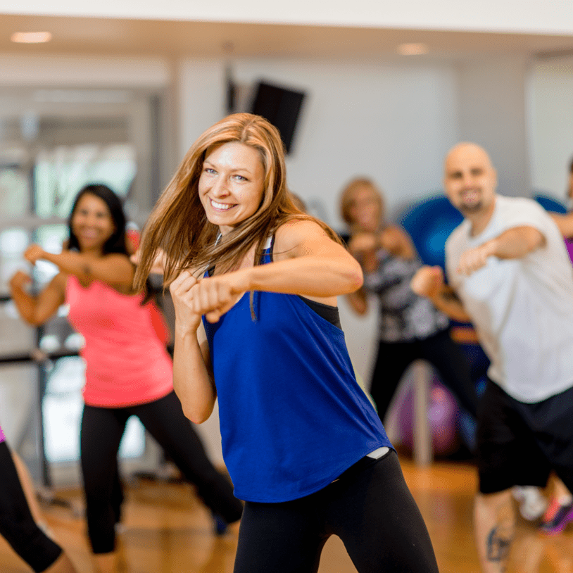 Eine Gruppe von f&uuml;nf Personen tanzt in einem Fitnessstudio, offensichtlich in einem Gruppentraining, l&auml;chelnd und motiviert.