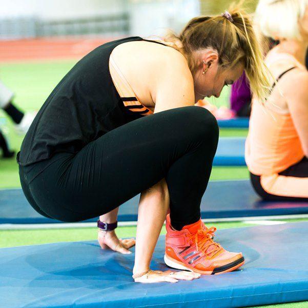 Eine Sportlerin &uuml;bt eine Dehn&uuml;bung auf einer blauen Matte in einer sportlichen Umgebung.