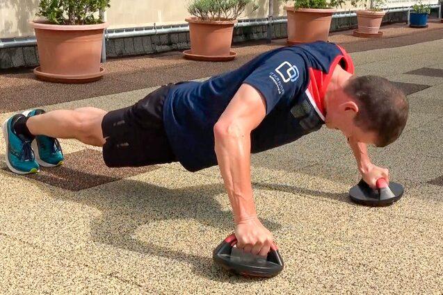 Mann f&uuml;hrt Liegest&uuml;tze auf einem Au&szlig;enterrassenboden mit Fitnessgriffen durch.