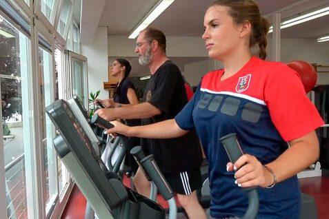 Drei Personen trainieren auf Crosstrainern in einem Fitnessstudio mit gro&szlig;en Fenstern.