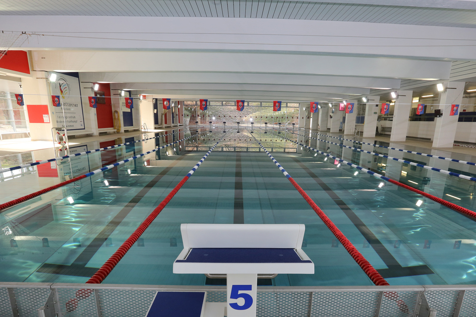 Blick auf ein Schwimmbecken mit mehreren Bahnen und einer Startbl&ouml;cke in einem hellen, modernen Hallenbad.