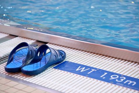 Blaue Badeschlappen liegen am Beckenrand eines Schwimmbeckens neben einem Hinweis auf die Wassertiefe von 1,93 m.