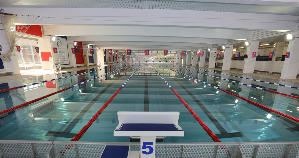 Blick auf ein Schwimmbecken mit mehreren Bahnen und einer Startbl&ouml;cke in einem hellen, modernen Hallenbad.