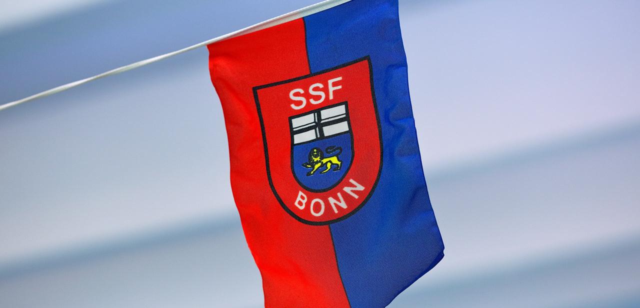 Flagge des SSF Bonn mit rotem und blauem Design, Wappen und Schriftzug "SSF BONN" in der Mitte.