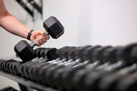 Eine Hand h&auml;lt eine Kurzhantel &uuml;ber einer Reihe von Kurzhanteln auf einem Gestell.