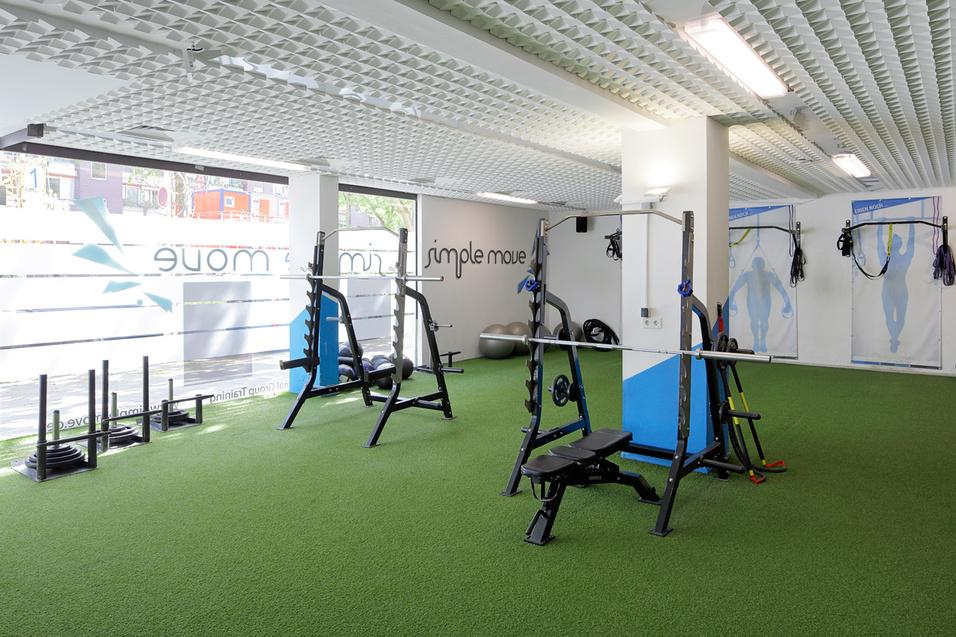 Fitnessstudio mit verschiedenen Trainingsger&auml;ten auf gr&uuml;nem Kunstrasenboden und gro&szlig;en Fenstern zur nat&uuml;rlichen Beleuchtung.