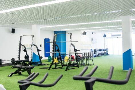 Innenansicht eines modernen Fitnessstudios mit freien Gewichten, Trainingsger&auml;ten und Kunstrasenboden.