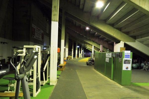 Blick auf eine Trainingshalle mit Fitnessger&auml;ten und einem langen Gang, beleuchtet durch Deckenlichter.
