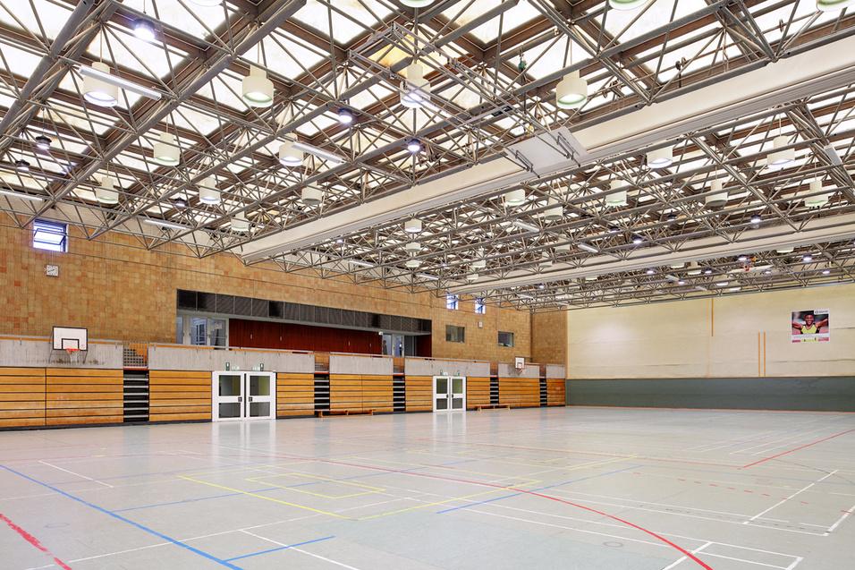 Helle Sporthalle mit Holzb&auml;nken, Basketballkorb und farblich markierten Spielfeldlinien auf dem grauen Boden.