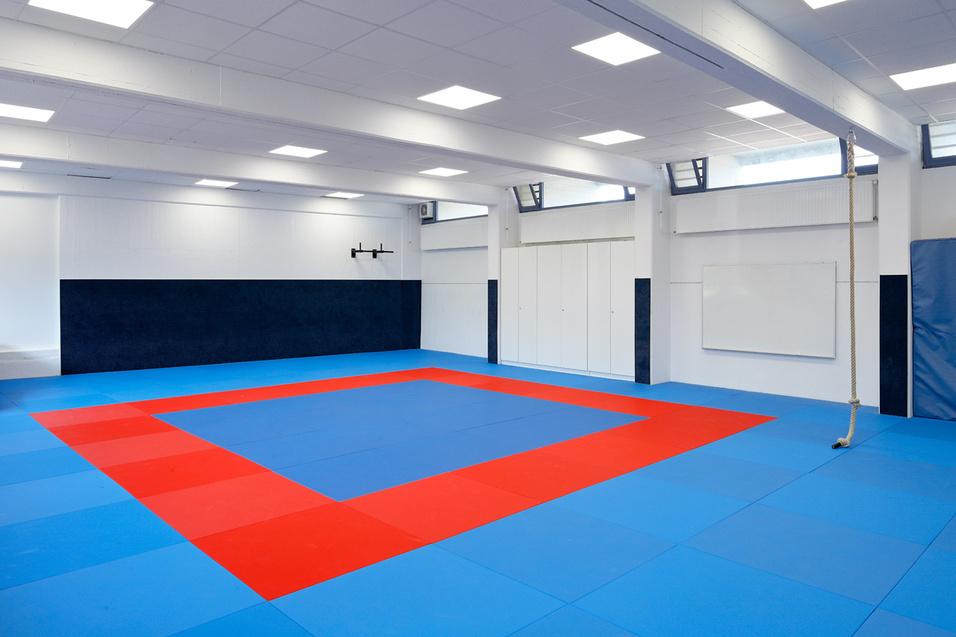 Leere Trainingshalle mit blauen und roten Matten und einem wei&szlig;en Bereich an der Wand.