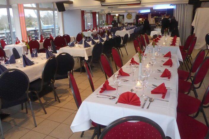 Elegant dekorierter Restaurantbereich mit wei&szlig; eingedeckten Tischen und roten sowie blauen Servietten.