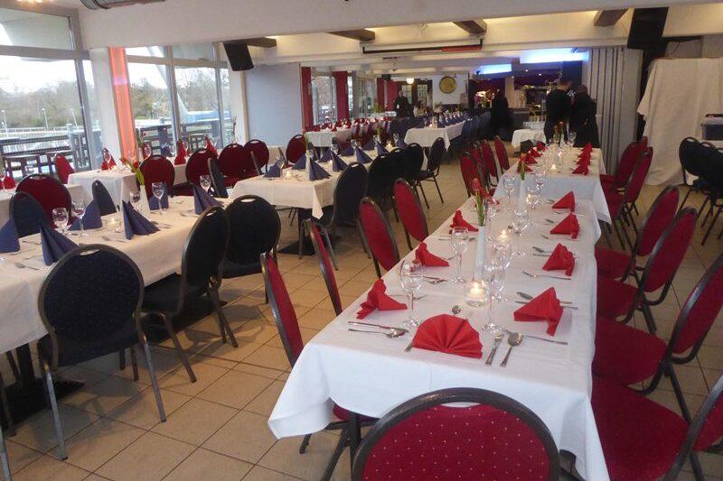 Elegant dekorierter Restaurantbereich mit wei&szlig; eingedeckten Tischen und roten sowie blauen Servietten.