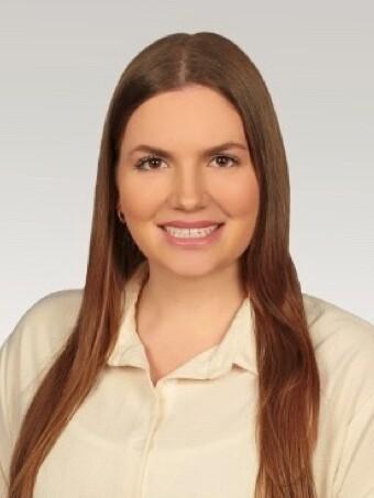 Portr&auml;t einer l&auml;chelnden Frau mit langen, glatten Haaren, tr&auml;gt ein helles Shirt vor einem neutralen Hintergrund.