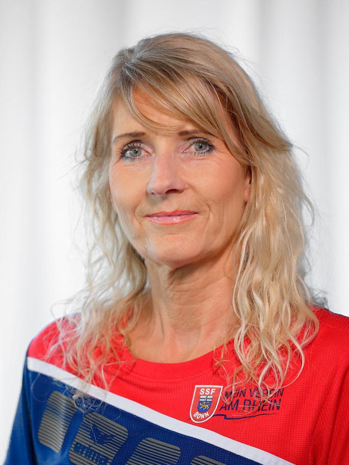 Portr&auml;t einer Frau mit langen, blonden Haaren, die ein rotes Sporttrikot tr&auml;gt, vor einem neutralen Hintergrund.