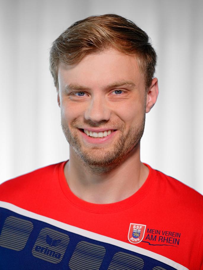 Portr&auml;t eines l&auml;chelnden jungen Mannes in einem sportlichen Trikot mit dem Aufdruck &bdquo;Mein Verein am Rhein&ldquo; vor hellem Hintergrund.