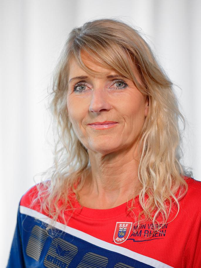 Portr&auml;t einer Frau mit langen, blonden Haaren, die ein rotes Sporttrikot tr&auml;gt, vor einem neutralen Hintergrund.