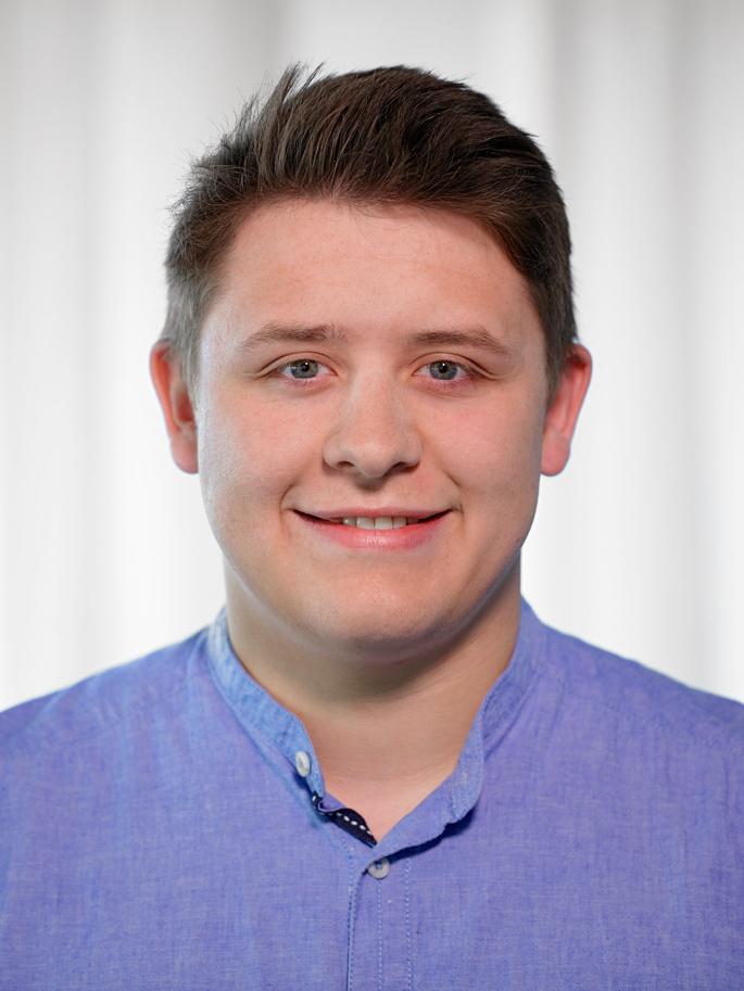 Portr&auml;t eines l&auml;chelnden jungen Mannes mit hellblauem Hemd vor einem neutralen, hellen Hintergrund.