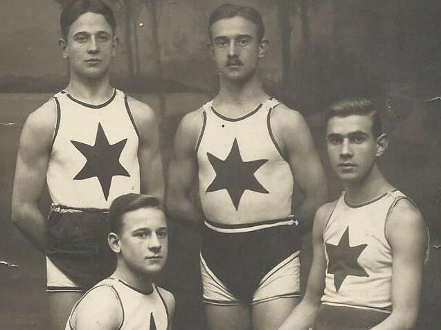 Vier sportlich gekleidete M&auml;nner in Schwimmanz&uuml;gen mit Sternenposen vor einer stilisierten Kulisse.
