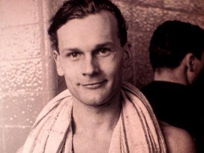 Junger Mann mit Handtuch um den Hals schaut freundlich in die Kamera, im Hintergrund schemenhafte Personen.