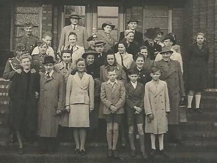 Gruppenfoto vor einem Geb&auml;ude, das eine Vielzahl von M&auml;nnern und Frauen in formeller Kleidung zeigt.