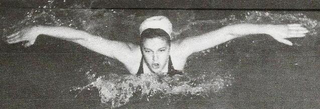 Schwimmerin im Wasser w&auml;hrend des Schmetterlingsstils mit ausgestreckten Armen und entschlossenem Gesichtsausdruck.