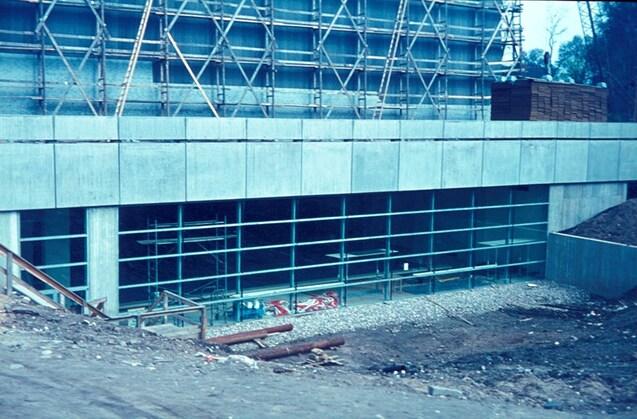 Bauprojekt mit Glasfront und Baustellenschutz, umgeben von Erdarbeiten und Ger&uuml;sten.