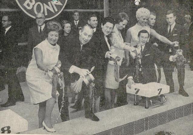 Menschen stehen auf einer B&uuml;hne mit Holzrennen in B&ouml;gen, w&auml;hrend sie kleine Reifen mit Schn&uuml;ren halten.