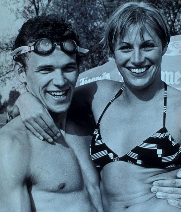 Zwei fr&ouml;hliche Schwimmer stehen nebeneinander, der Mann tr&auml;gt Schwimmbrille, die Frau einen gestreiften Bikini.