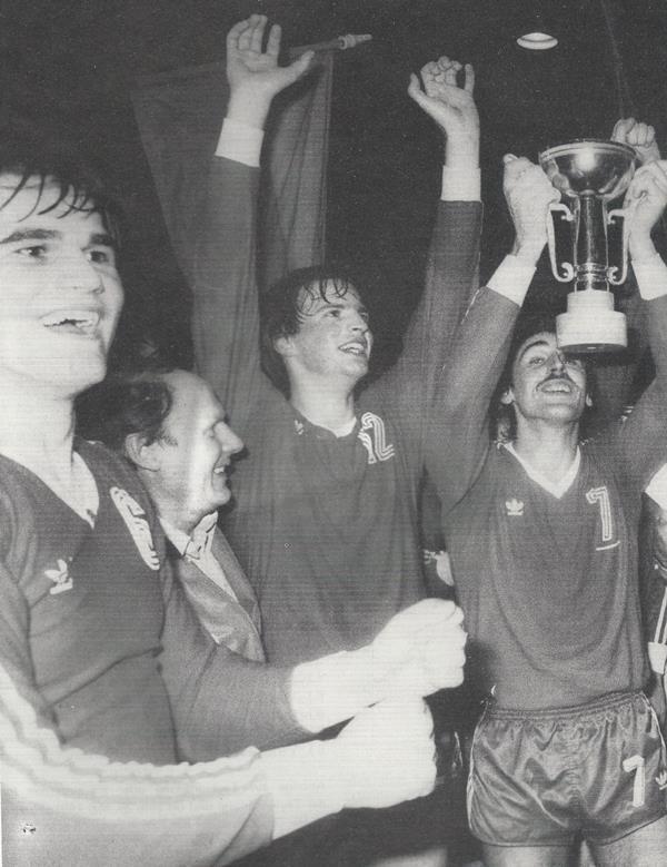 F&uuml;nf jubelnde M&auml;nner in Sporttrikots halten einen Pokal hoch und feiern einen Sieg.