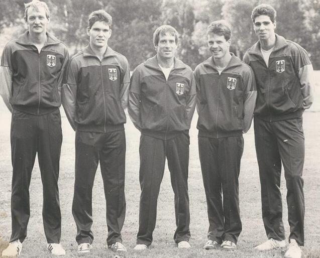 F&uuml;nf Athleten in Trainingsanz&uuml;gen mit Deutschlandwappen stehen auf einem Rasenplatz und posieren freundlich f&uuml;r das Foto.
