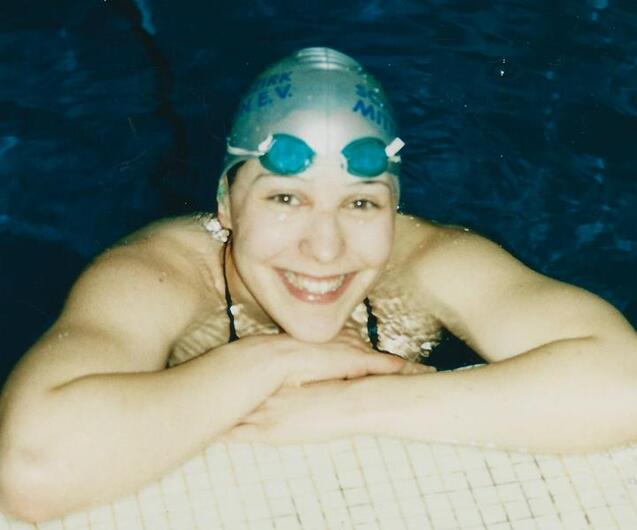 L&auml;chelnde Schwimmerin mit Badekappe und Schwimmbrille lehnt am Beckenrand in einem Schwimmbecken.