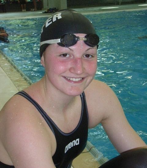 L&auml;chelnde Schwimmerin mit Badekappe und Schwimmbrille sitzt am Beckenrand eines Schwimmbades.