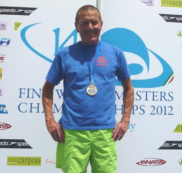 L&auml;chelnder Mann mit Medaille, blauer T-Shirt und gr&uuml;nen Shorts vor einem Hintergrund mit Wettkampf-Logos.