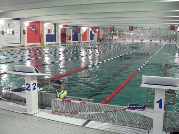 Schwimmhalle mit mehreren Bahnen, Schwimmern und orange-roten Markierungen an den Beckenr&auml;ndern.