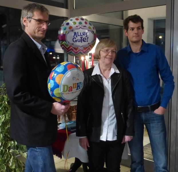 Drei Personen stehen vor Fenstern, halten Luftballons mit den Aufschriften &bdquo;Alles Gute&ldquo; und &bdquo;Danke&ldquo;.