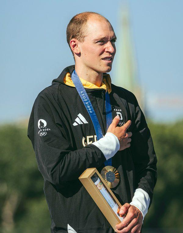 Sportler mit Goldmedaille und Ehrung auf dem Podium, h&auml;lt eine Auszeichnung und zeigt Stolz in strahlendem Licht.