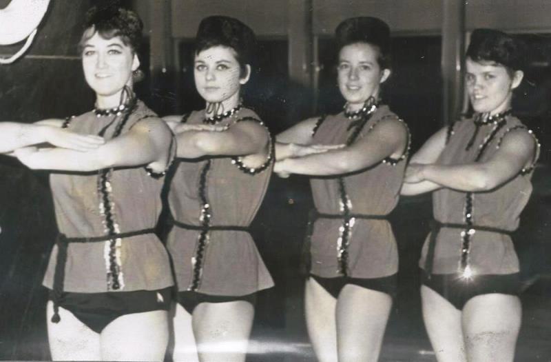 Vier Frauen in gl&auml;nzenden, rot-schwarzen Kost&uuml;men posieren synchron in einer Tanzauff&uuml;hrung.