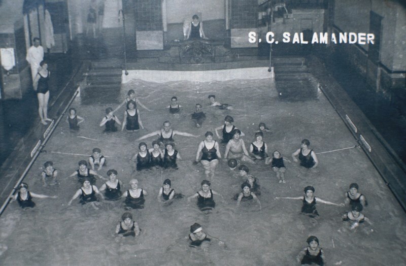 Schwarz-Wei&szlig;-Foto einer Schwimmgruppe in einem Hallenbad, Frauen in Badeanz&uuml;gen schwimmen und spielen Ball.