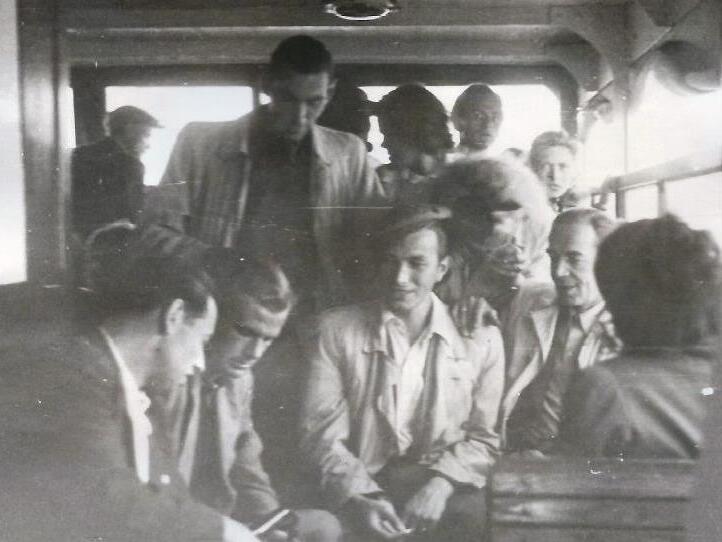 Gruppe von Menschen in einem Fahrzeug, einige sitzen, andere stehen und unterhalten sich lebhaft.