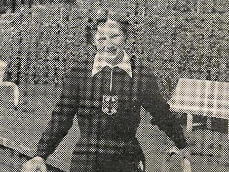 Frau in sportlicher Kleidung steht l&auml;chelnd an einem Schwimmbecken mit Haltegriffen. Hintergrund zeigt unkenntliche B&auml;ume.