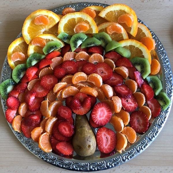 Bunt dekorierte Obstplatte mit Scheiben von Orange, Kiwi, Mandarine, Erdbeere und einer Birne in der Mitte.