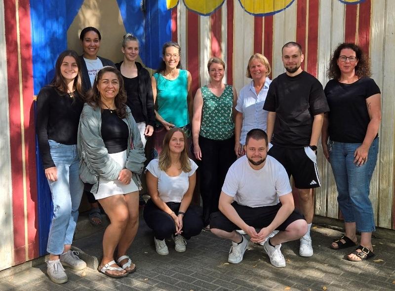 Gruppe von zw&ouml;lf Personen posiert vor einer bunten Wand mit roten und blauen Streifen.