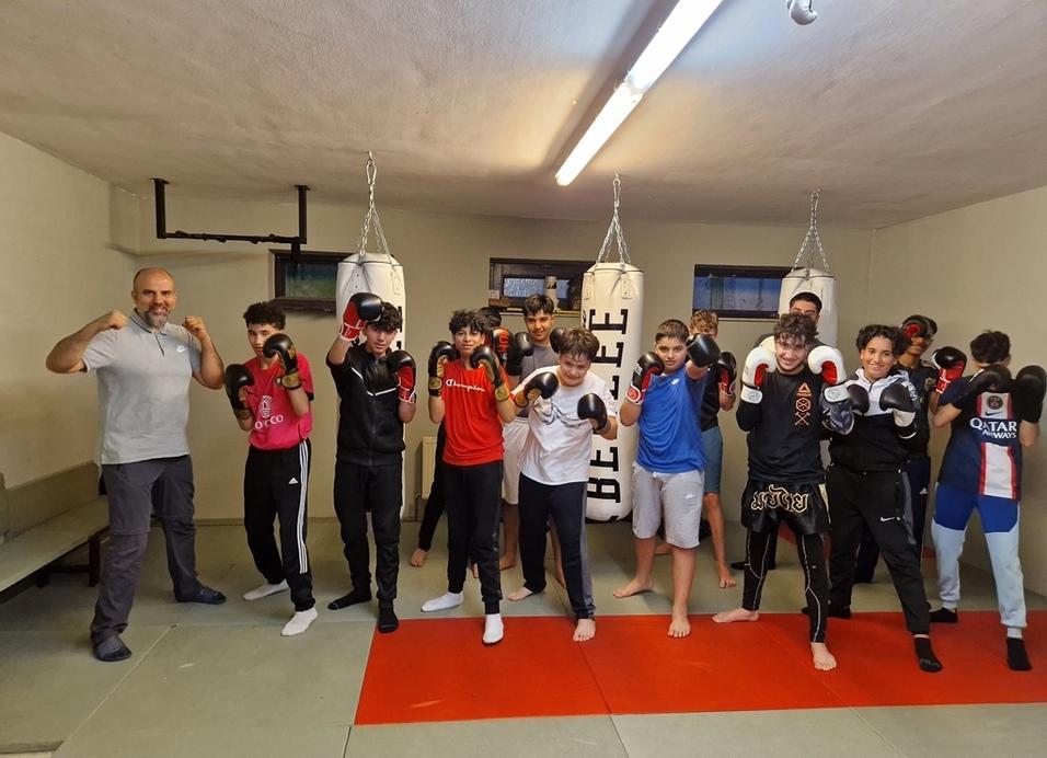 Gruppe von Jugendlichen in einem Boxraum, mit Boxhandschuhen und Boxs&auml;cken, posierend f&uuml;r ein Gruppenfoto.